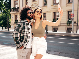 Smiling beautiful woman and her handsome boyfriend. Sexy cheerful family having tender moments in the street at sunset. Models hugging. Embracing each other. Love concept. In sunglasses. Taking selfie