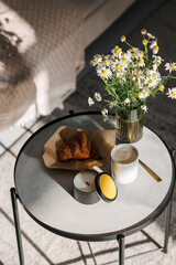 Morning Breakfast with fresh French croissants and cappuccino. A bouquet of daisy flowers and a wax candle in a tin. Sunny spring, summer mood. Serving concept.