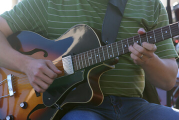 A man in a green and white striped T-shirt and denim jeans plays the electric guitar