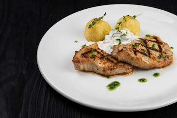 Grilled pork meat with mushroom sauce and potato on white plate on wooden black background