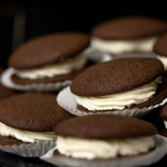 Chocolate sandwich cookies with cream. Dessert on corrugated paper. Festive baking. Close-up. Soft focus. Side view. Dark background.