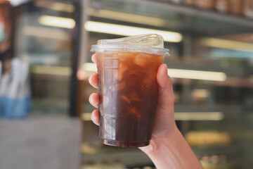 Close up of Hand holding a glass of Iced Americano or balck coffee with coffee shop in background. Concept of promoted coffee shop or cafe with copy space and wide screen.