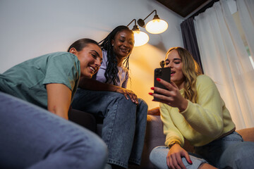 Friends hanging out at home, one friend is showing something on her phone to others. Low angle shot