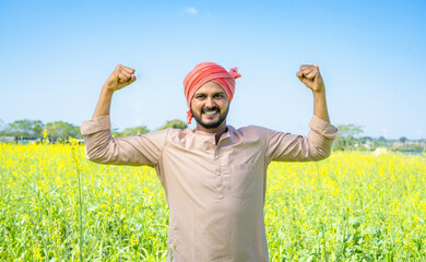 Happy famer showing stroing gesture using two hands at farmland by looking at camera - conept of...