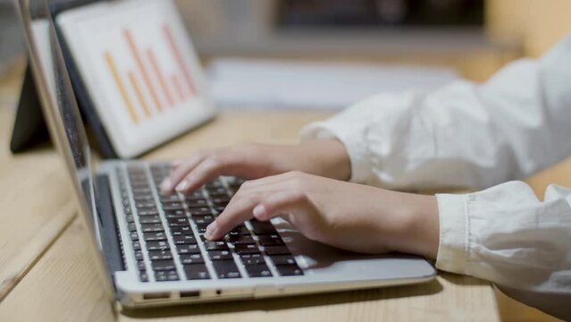 Closeup shot of schoolchild typing on laptop, doing homework in the evening. Kid writing essay or preparing report based on bar chart shown on tablet screen. Modern technology, education concept