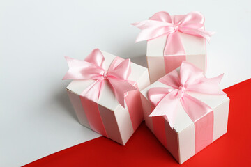 Three gift boxes with pink satin ribbon on white and red background.