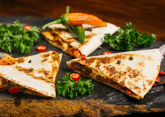 Quesadilla with chicken and hot peppers, curly parsley leaves and two bottles of hot sauce.