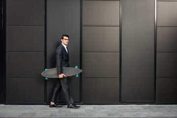 Young handsome man with business suit riding on a longboard - Corporate businessman portrait, concepts about business, mobility and lifestyle