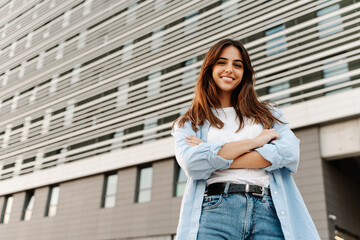 Confident young caucasian woman standing in the city looking to the camera with smile