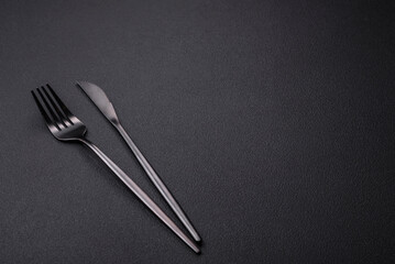 Metal kitchen knife and fork on a dark textured concrete background