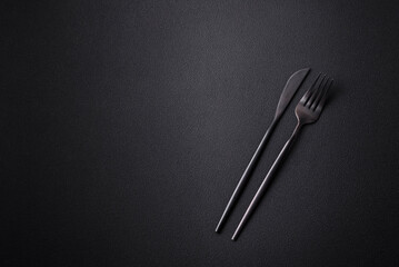 Metal kitchen knife and fork on a dark textured concrete background