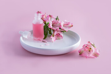 an open bottle of frosted glass with cosmetics and a filled pipette on a white ceramic plate with delicate spring flowers. care for young skin.