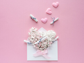 Ein Briefkuvert gefüllt mit weißen Blüten und kleinen Wunschzetteln. Flat lay, rosa Hintergrund.