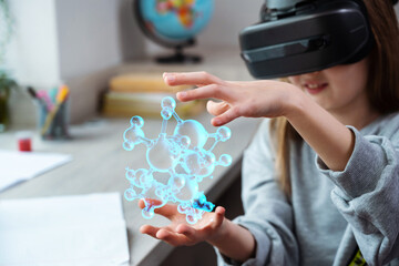 Schoolgirl using VR headset simulators for studying. Child is wearing virtual reality glasses sits at desk watching the structure of the water molecule. Future learning concept