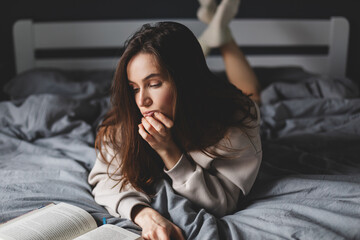 Charming caucasian lady lying in bed, reading a book, she look boring and tired.