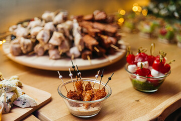 Meat canapés of chicken in walnut sauce, assortment of meat kebabs on large wooden skewers, caprese canapes in pesto sauce on the buffet table