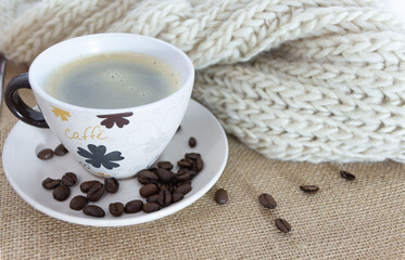 A warm cup of coffee over a jute tablecloth, with some coffee beans over the table. Cozy cafeteria.