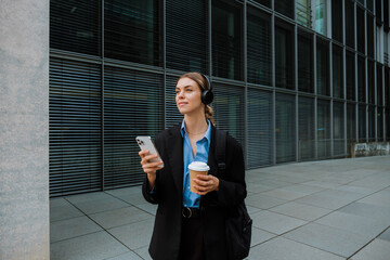 Young woman wearing headphones using smartphone while walking outdoors