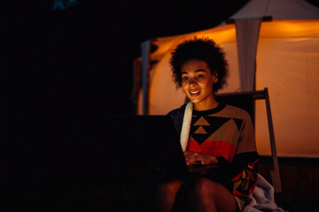 Young woman using laptop while sitting by tent in forest at night © Drobot Dean