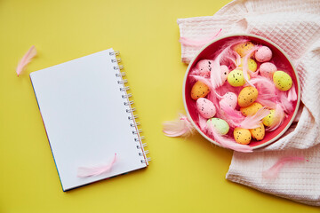 Creative bright Easter notepad mock up on yellow background. Decorated Easter: pink bowl with colorful eggs and pink feathers.