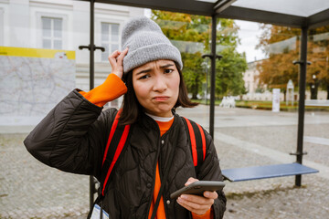 Confused asian woman using smartphone while standing at bus station © Drobot Dean