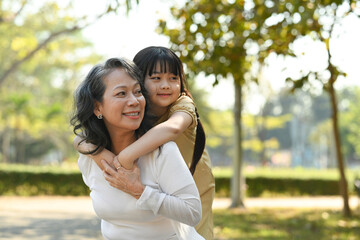 Image of smiling idle age grandmother giving piggyback ride to cute little granddaughter during...