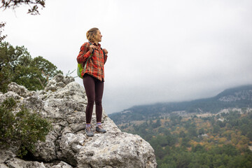 Naklejka premium traveler girl stands on the edge of a cliff with an autumn forest and enjoys a beautiful view of the valley.