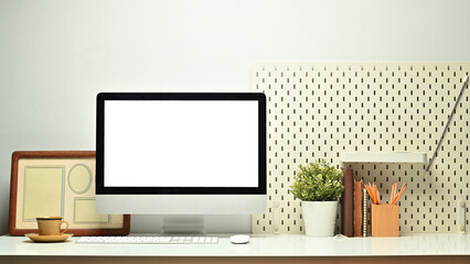 Front view of white blank screen computer monitor, picture frame, pencil holder and houseplant on working table