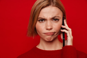 Young blonde woman with short hair frowning while talking on cellphone