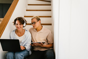 Two multinational colleagues with tablet and laptop working together while sitting on stairs