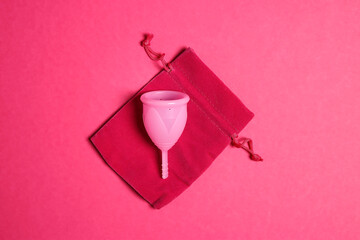 Menstrual cup with storage pouch on pink background.
