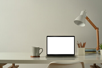 Front view of laptop computer, coffee cup, pencil holder and lamp on white table in minimal home...