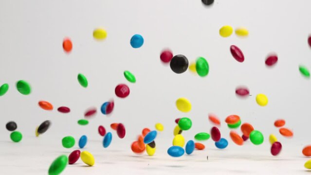 Bright colored chocolate m and m candies bouncing, dancing and spinning on white table top in slow motion