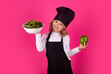 Kid cook with avocado and vegetable. Kid chef cook prepares food on isolated studio background. Kids cooking. Teen boy with apron and chef hat preparing a healthy meal.