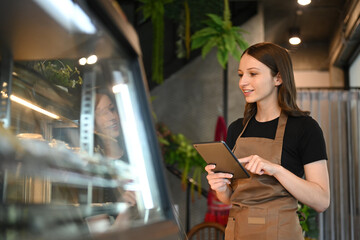 Beautiful caucasian woman coffee shop owner using tablet and checking inventory in a cozy cafe interior
