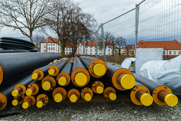Black  isolated heating large pipes with yellow plastic plugs lie on a construction site.