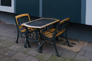 Cast iron benches and a table of a street cafe closed with a chain.