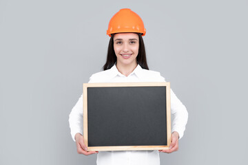 Young woman in helmet hold board on gray background. Architect businesswoman in helmet thinking, young caucasian female in work as constructor engineer.