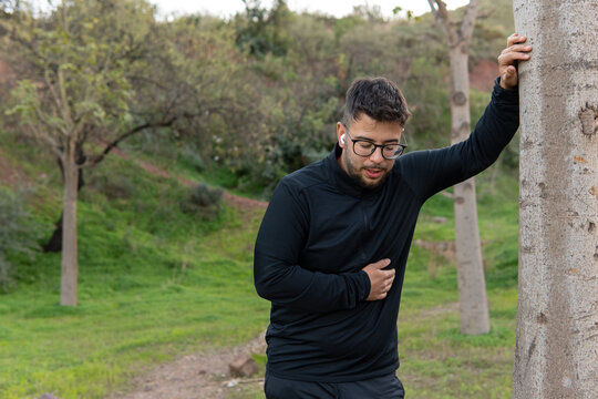 Tired young man leaning against a tree after jogging in the park