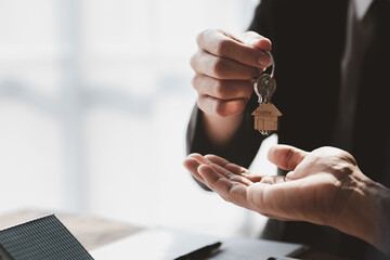 A home rental company employee is handing the house keys to a customer who has agreed to sign a rental contract, explaining the details and terms of the rental. Home and real estate rental ideas.