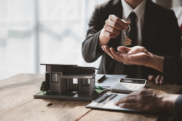 A home rental company employee is handing the house keys to a customer who has agreed to sign a...