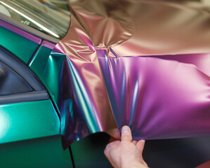 A specialist in wrapping a car with chameleon-colored vinyl film in the process of work. Car...