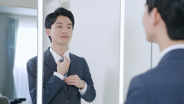 洗面所で鏡を見てネクタイを締める若いビジネスマン（朝・出勤準備）