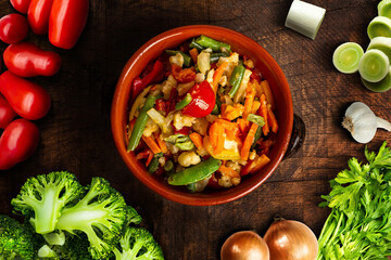 Mediterranean Vegetables in terracotta dish on old wooden table. Natural nutrition concept. Top view.