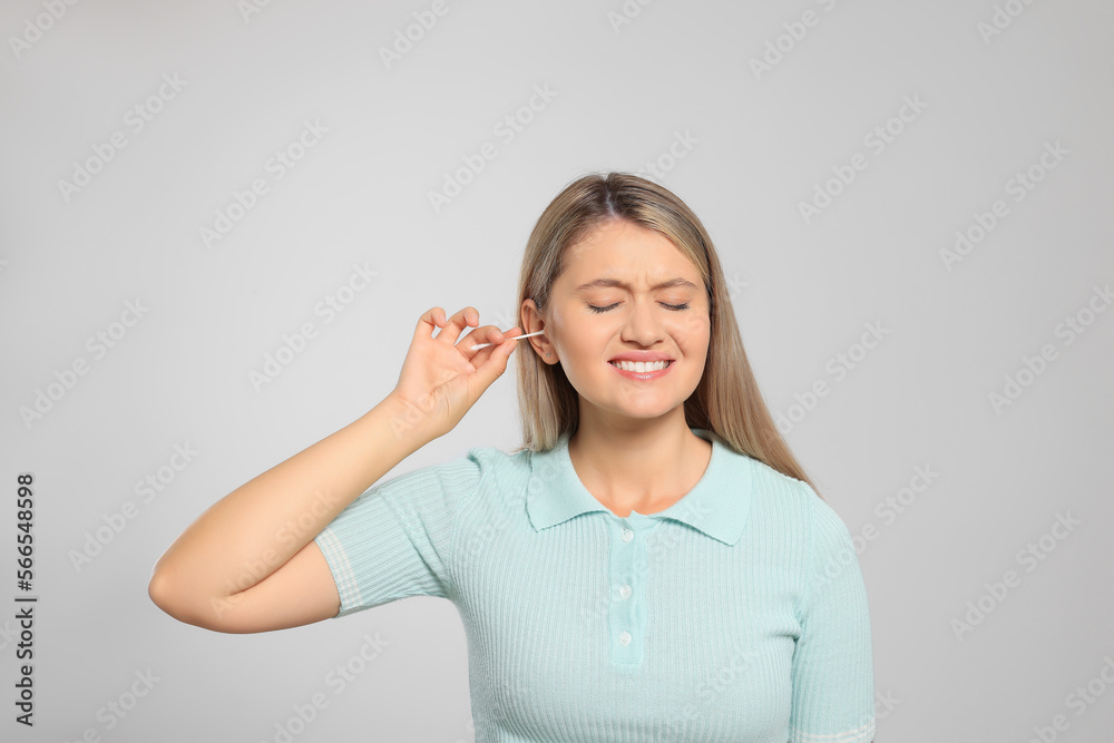 Sticker Young woman cleaning ear with cotton swab on light grey background