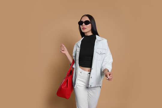 Young woman with stylish bag on beige background