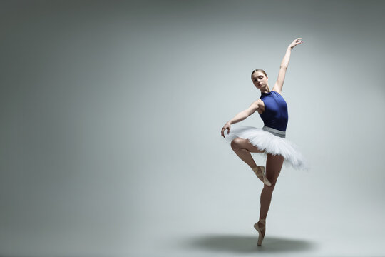 Young ballerina practicing dance moves on grey background. Space for text