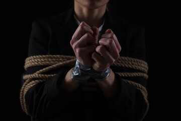 Woman tied up and taken hostage on dark background, closeup