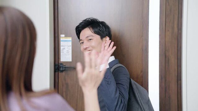 出勤する夫と玄関で見送る妻（夫婦・カップル・行ってらっしゃい・バイバイ）