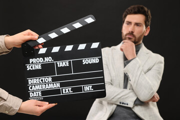 Actor performing while second assistant camera holding clapperboard on black background, closeup - obrazy, fototapety, plakaty